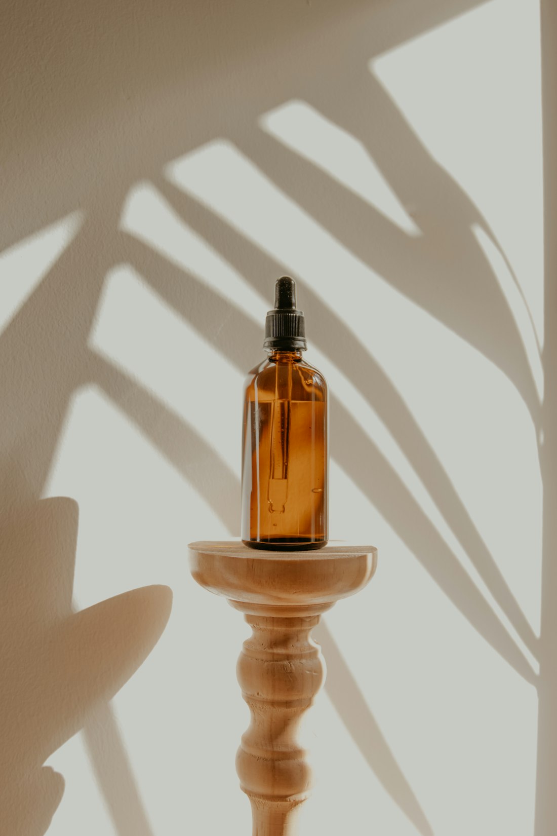 Gift A Spa — an amber bottle of massage oil on a turned wooden stand, palm-leaf shadows across the wall