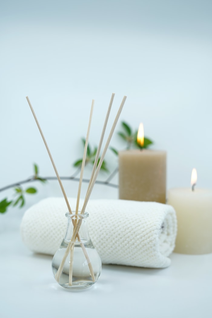 A reed diffuser and lit candles beside a rolled towel.